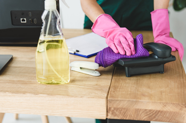 cleaner wiping down office phone on desk with cloth