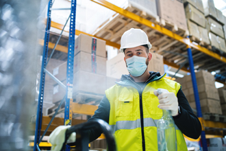 warehouse worker cleaning industrial shelves and equipment with disinfectant spray, wearing face mask