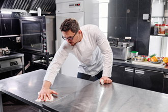 restaurant chef wiping down metal kitchen tops in kitchen