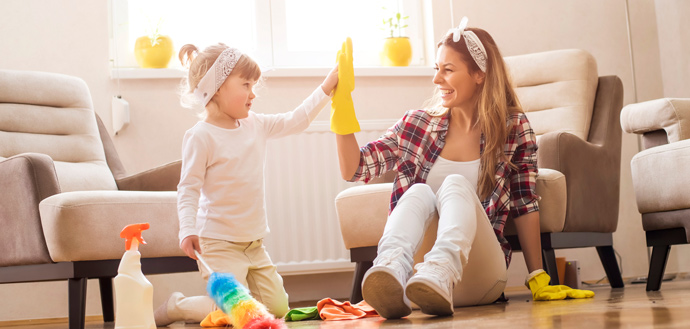 mother and young daughter high-fiving sitting on living room floor with cleaning products, happy concept of completion