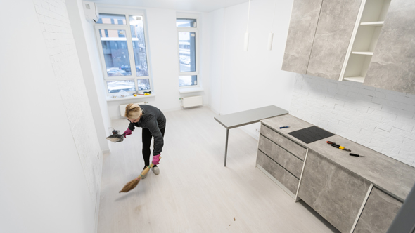 woman cleaning up construction dust in new room of property, dustpan and brush