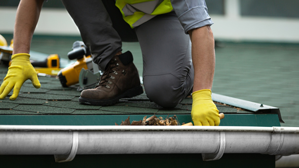 tradesman clearing gutter of leaves, build up