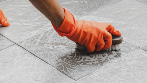 cleaner using bristle brush to clean floor tiles, close up